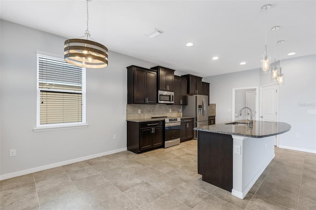 kitchen with pendant lighting, stainless steel appliances, a kitchen island with sink, and sink