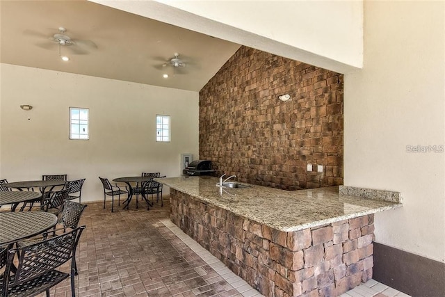 bar featuring light stone countertops, vaulted ceiling, ceiling fan, and sink