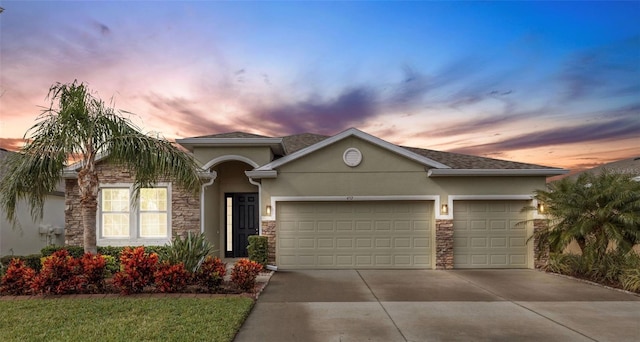 view of front of home with stucco siding, driveway, stone siding, and a garage