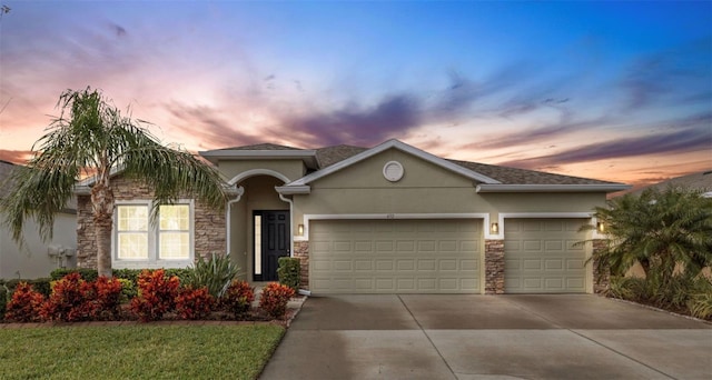 view of front of home with stucco siding, driveway, stone siding, and a garage