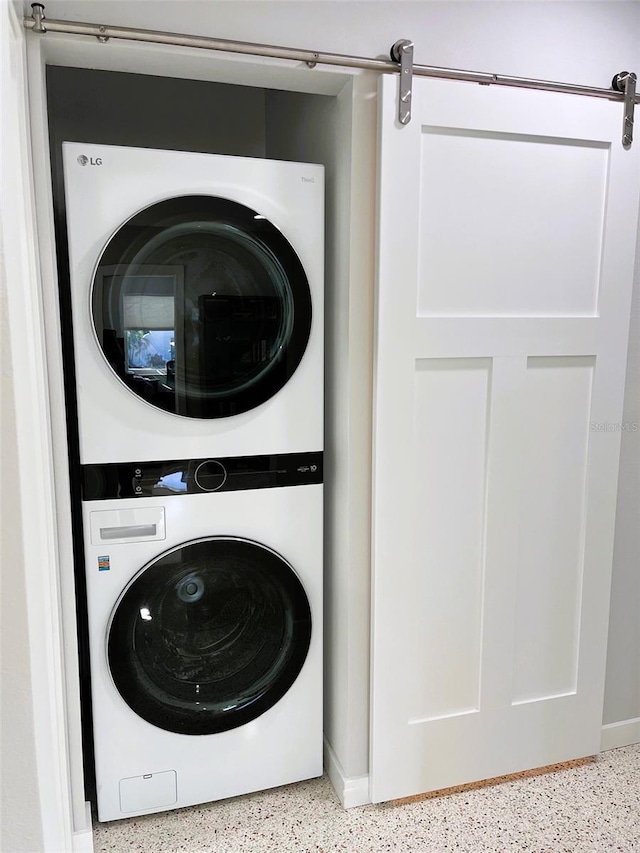 clothes washing area featuring a barn door and stacked washer / drying machine