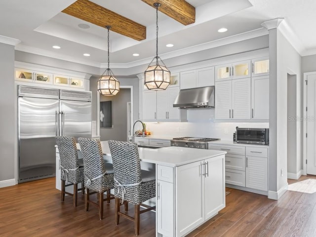 kitchen with exhaust hood, pendant lighting, stainless steel built in fridge, white cabinetry, and an island with sink