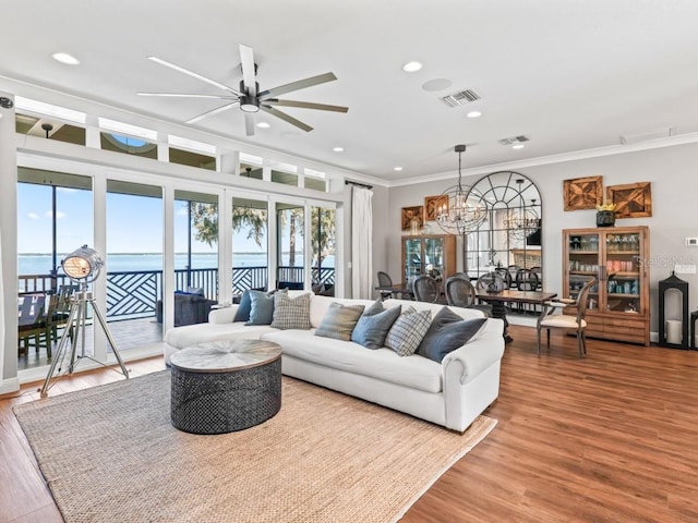 living room with ceiling fan with notable chandelier, a water view, wood-type flooring, and crown molding