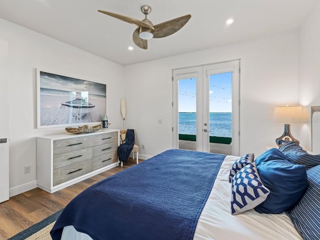 bedroom featuring access to outside, ceiling fan, a water view, and dark wood-type flooring