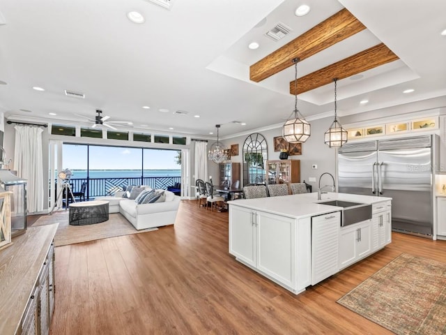 kitchen with white cabinetry, sink, hanging light fixtures, built in refrigerator, and a center island with sink