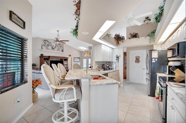 kitchen with kitchen peninsula, appliances with stainless steel finishes, a kitchen bar, light stone countertops, and backsplash