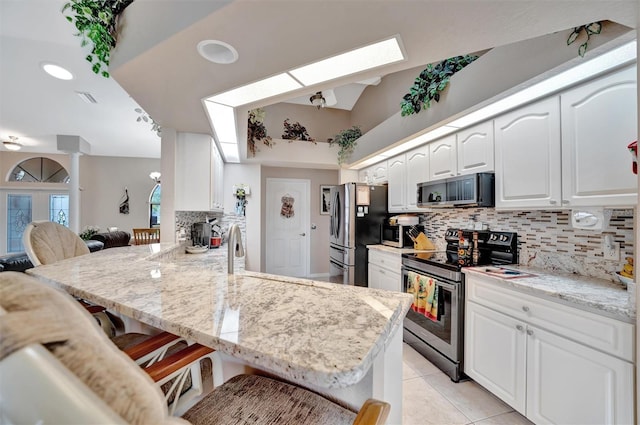 kitchen with a breakfast bar, white cabinets, appliances with stainless steel finishes, tasteful backsplash, and kitchen peninsula