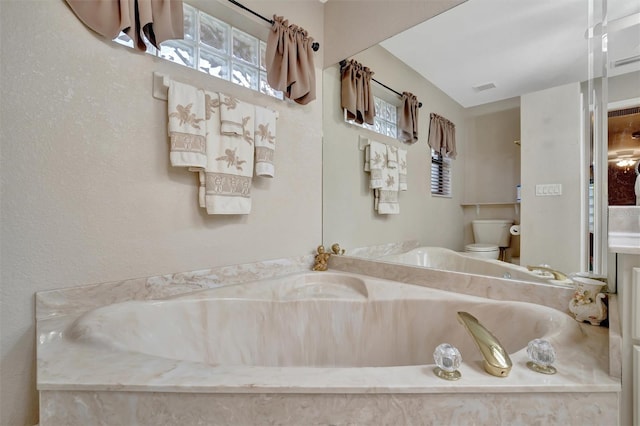 bathroom featuring tiled bath and toilet