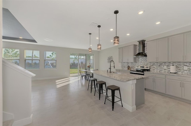 kitchen featuring gray cabinetry, stainless steel range, sink, wall chimney range hood, and a kitchen island with sink