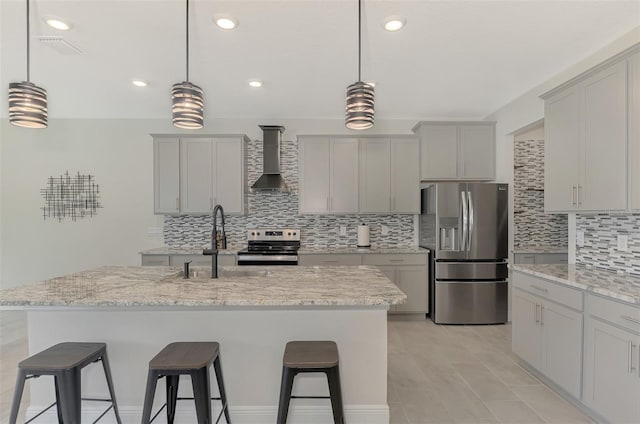 kitchen with light stone countertops, an island with sink, stainless steel appliances, and wall chimney range hood