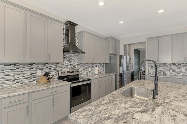 kitchen with light stone countertops, wall chimney range hood, sink, and appliances with stainless steel finishes