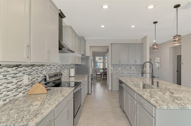 kitchen featuring appliances with stainless steel finishes, light stone counters, sink, hanging light fixtures, and an island with sink