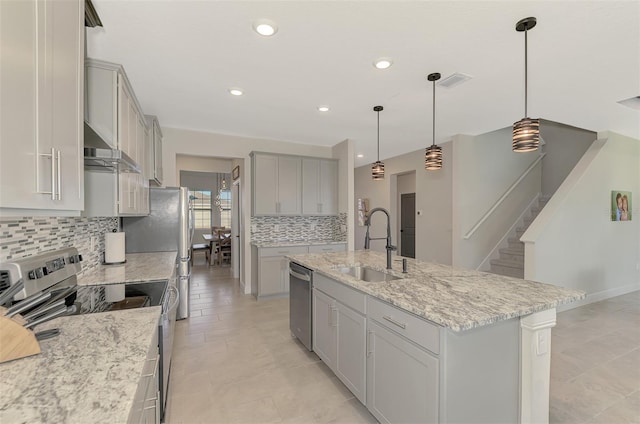 kitchen featuring backsplash, stainless steel appliances, exhaust hood, decorative light fixtures, and an island with sink