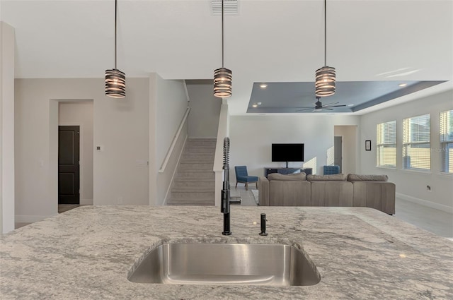 kitchen featuring light stone counters, a tray ceiling, ceiling fan, sink, and hanging light fixtures