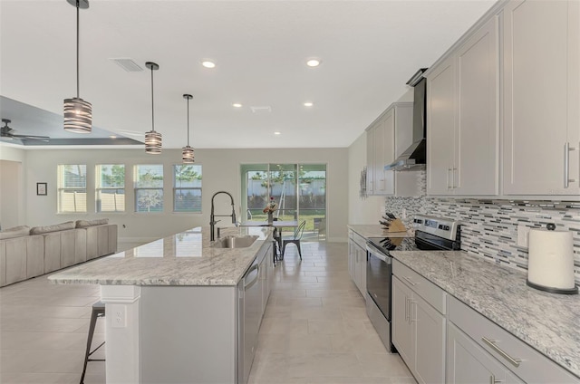 kitchen with a kitchen island with sink, wall chimney range hood, sink, ceiling fan, and appliances with stainless steel finishes