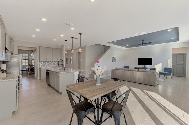 dining area with a raised ceiling, ceiling fan, sink, and light tile patterned floors