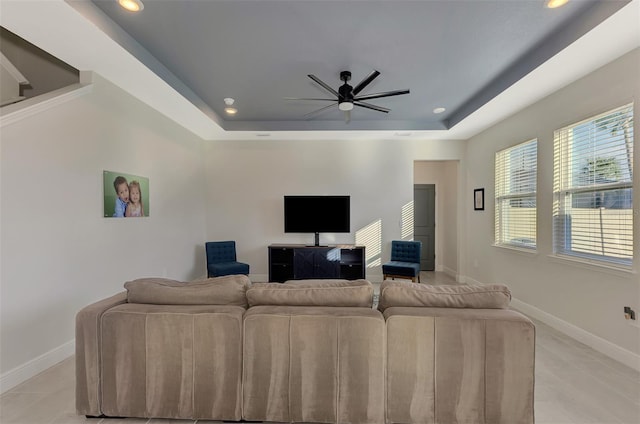 tiled living room with ceiling fan and a raised ceiling