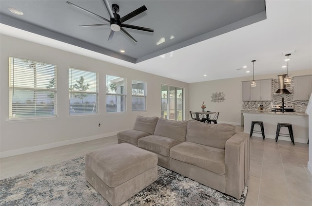 living room featuring a raised ceiling, ceiling fan, and light tile patterned floors