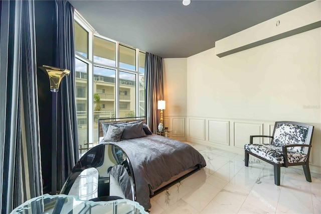 bedroom with marble finish floor, floor to ceiling windows, wainscoting, and a decorative wall