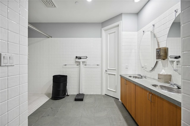 bathroom featuring tile walls, visible vents, a tile shower, and a sink