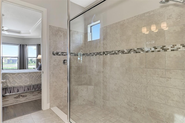 bathroom featuring tile patterned flooring, ceiling fan, a tile shower, and a tray ceiling