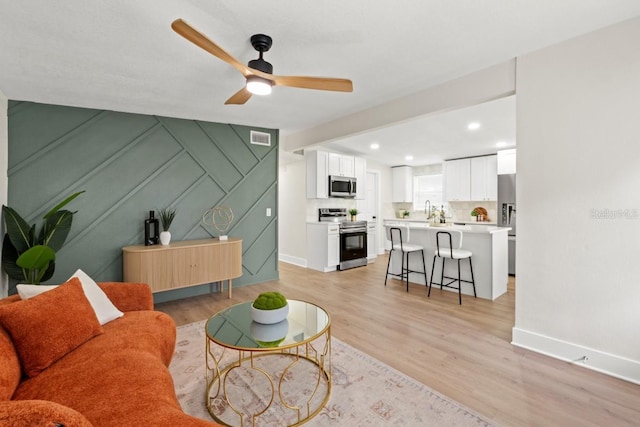 living room with ceiling fan, light hardwood / wood-style floors, and sink