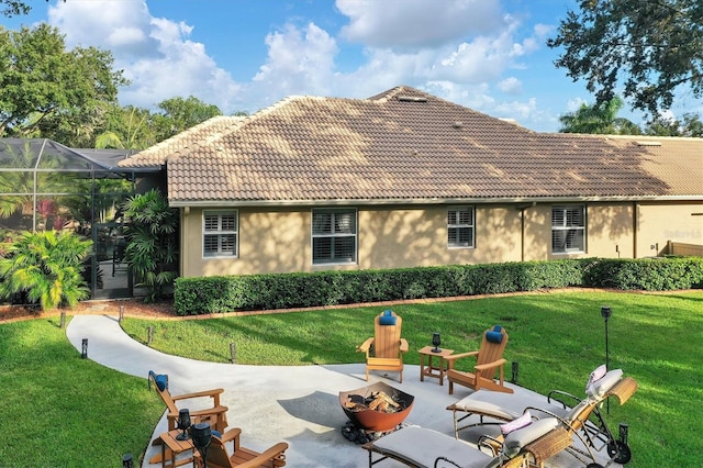 rear view of house with a lawn, glass enclosure, a patio, and an outdoor fire pit