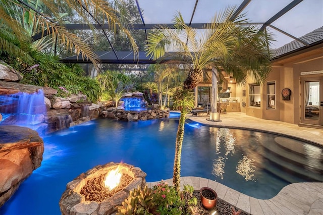 pool at dusk with glass enclosure, pool water feature, a patio area, and an outdoor fire pit