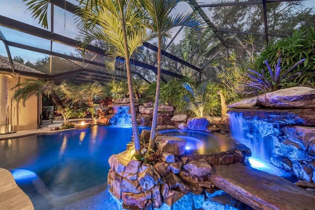 view of pool with an in ground hot tub, pool water feature, glass enclosure, and a patio area