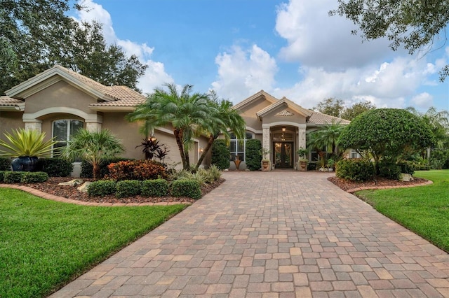 mediterranean / spanish house featuring a tiled roof, decorative driveway, a front yard, and stucco siding