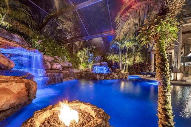 view of pool with a pool with connected hot tub, glass enclosure, and a fire pit