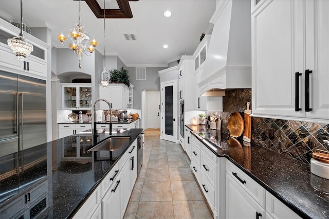 kitchen with glass insert cabinets, dark stone countertops, decorative light fixtures, premium range hood, and white cabinetry