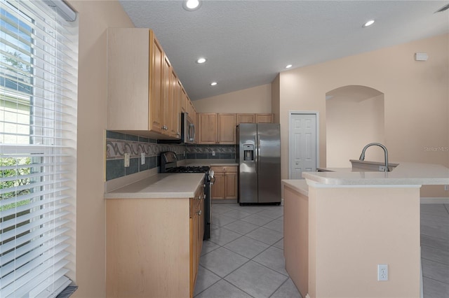 kitchen with lofted ceiling, a kitchen island with sink, decorative backsplash, light tile patterned flooring, and stainless steel appliances