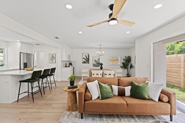 living room with ceiling fan with notable chandelier and light wood-type flooring