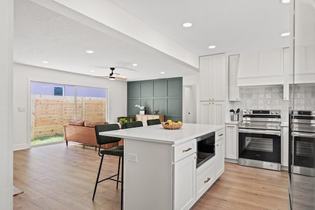 kitchen featuring a kitchen island, built in microwave, a breakfast bar area, white cabinets, and electric range