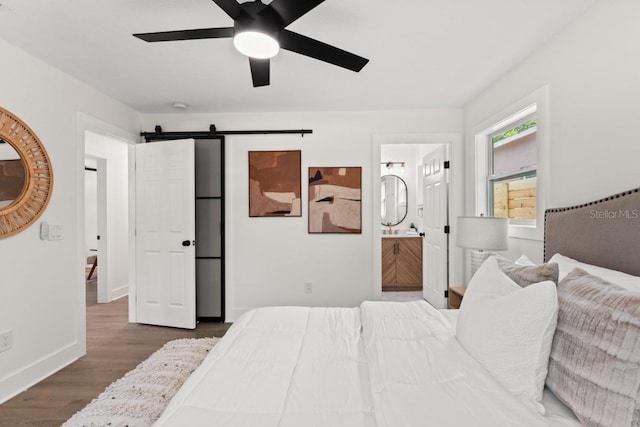 bedroom with dark hardwood / wood-style flooring, ensuite bath, a barn door, and ceiling fan