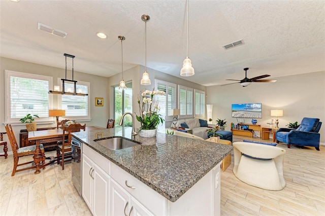 kitchen with white cabinetry, sink, dark stone counters, hanging light fixtures, and a kitchen island with sink