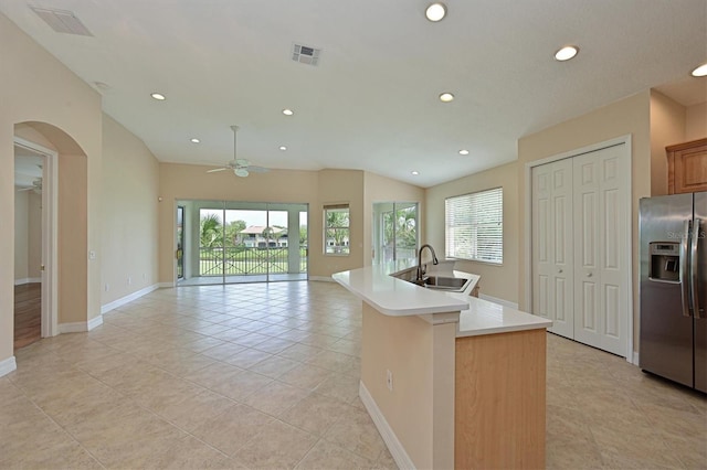 kitchen featuring ceiling fan, sink, stainless steel fridge, plenty of natural light, and a center island with sink