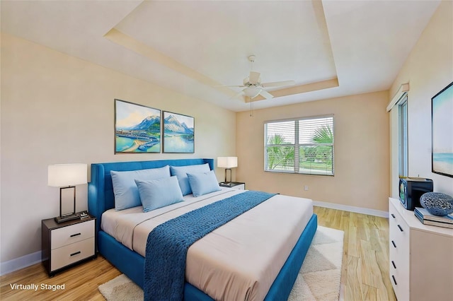 bedroom with a tray ceiling, ceiling fan, and light hardwood / wood-style flooring