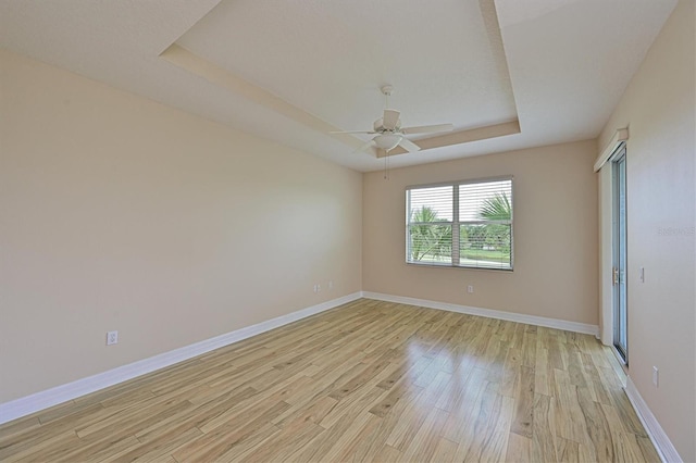 unfurnished room with a raised ceiling, ceiling fan, and light hardwood / wood-style flooring