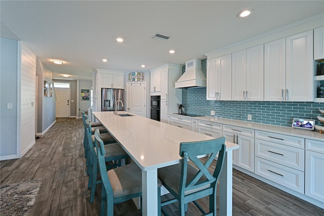 kitchen featuring custom exhaust hood, a breakfast bar, black appliances, white cabinets, and a large island