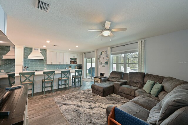 living room with ceiling fan, a textured ceiling, and light wood-type flooring