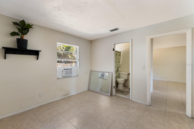 unfurnished bedroom with ensuite bathroom, cooling unit, light tile patterned floors, and a textured ceiling