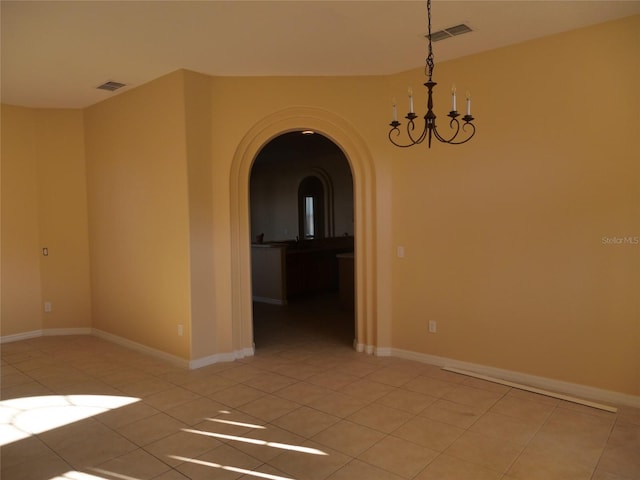 tiled spare room with a notable chandelier