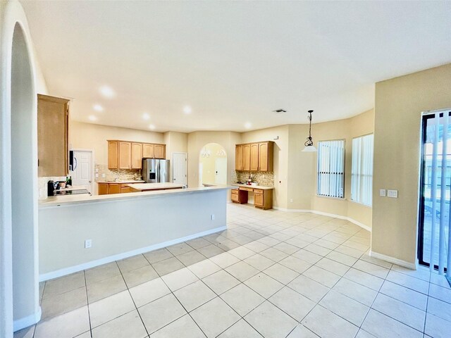 kitchen with stainless steel refrigerator with ice dispenser, decorative backsplash, arched walkways, and light countertops