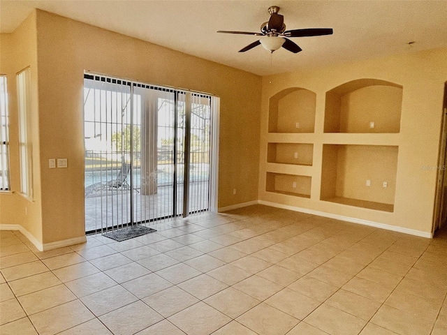 spare room featuring a ceiling fan, baseboards, built in shelves, and light tile patterned floors