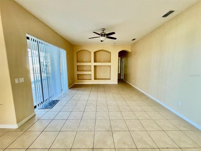 empty room featuring a ceiling fan, visible vents, built in features, arched walkways, and light tile patterned floors