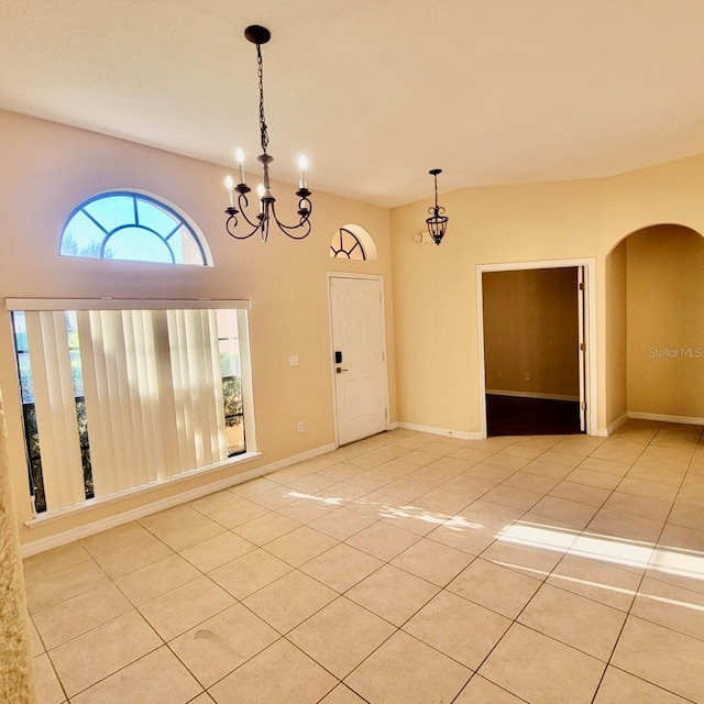unfurnished room with light tile patterned floors, arched walkways, an inviting chandelier, and baseboards