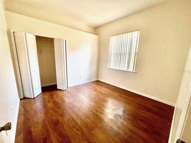 unfurnished bedroom featuring baseboards, wood finished floors, and a closet