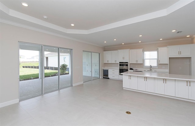 kitchen with a tray ceiling, beverage cooler, sink, white cabinets, and a kitchen island